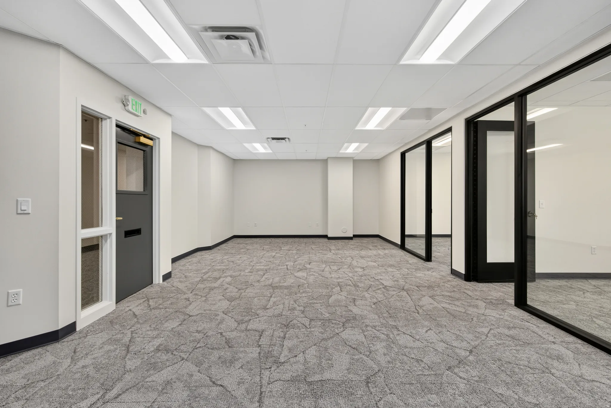 Expansive open-plan workspace featuring patterned carpeting, white walls, and a dropped ceiling with integrated lighting