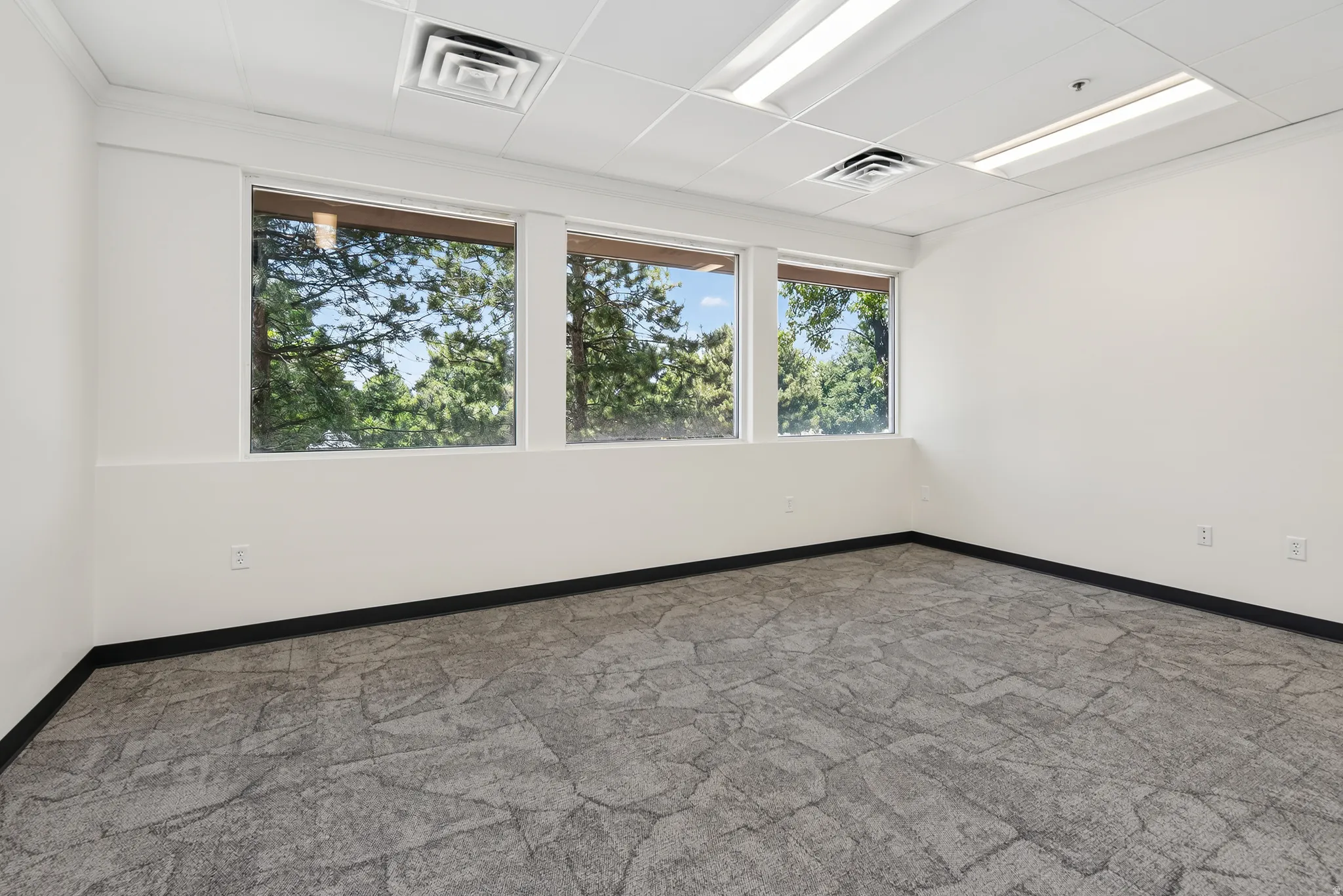 Interior space featuring three windows, neutral wall tones, drop ceiling, recessed lighting, and patterned carpet flooring