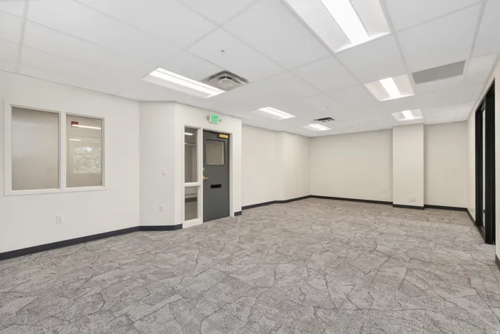 Spacious interior room with patterned carpet flooring, drop ceiling with recessed lighting, and white walls