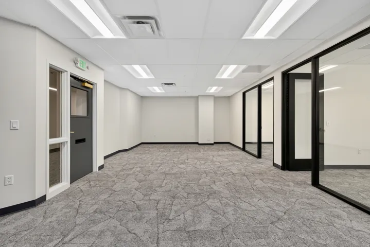 Expansive open-plan workspace featuring patterned carpeting, white walls, and a dropped ceiling with integrated lighting