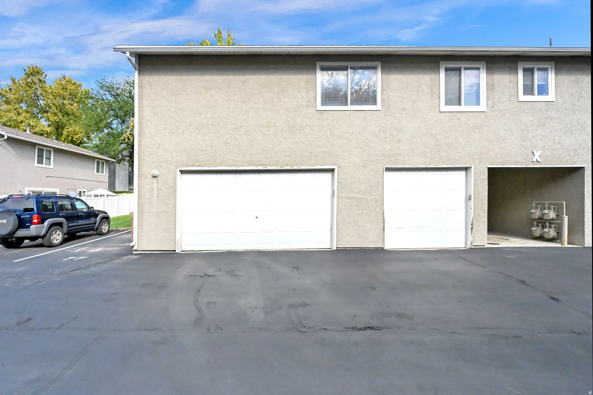 Stucco exterior with multiple windows, two garage doors, and an additional covered parking space