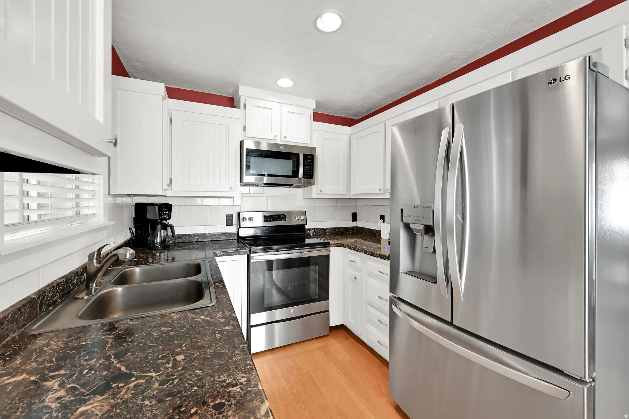 White cabinetry with stainless steel appliances, dark finish countertops, and wood-finish flooring