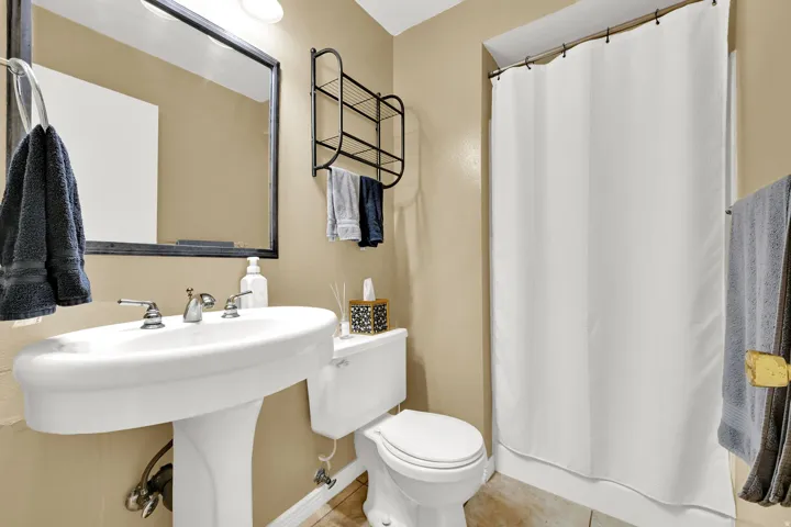 Pedestal sink with chrome fixtures, framed mirror, and a shower-tub combination