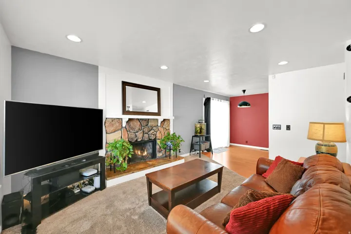 Stone-clad fireplace with mantel, recessed ceiling lights, and wood-finish flooring