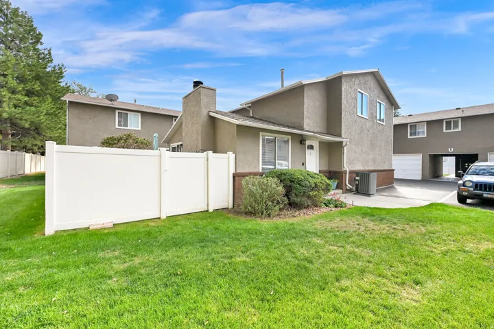 Stucco exterior with an attached chimney, established shrubbery, and a white privacy fence