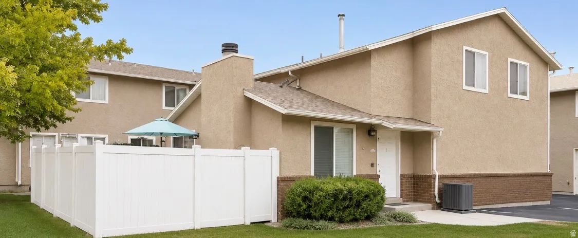 Exterior featuring stucco siding with a brick lower facade, gabled roofline, and white vinyl fencing