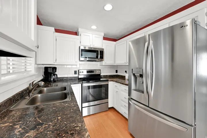 White cabinetry with stainless steel appliances, dark finish countertops, and wood-finish flooring