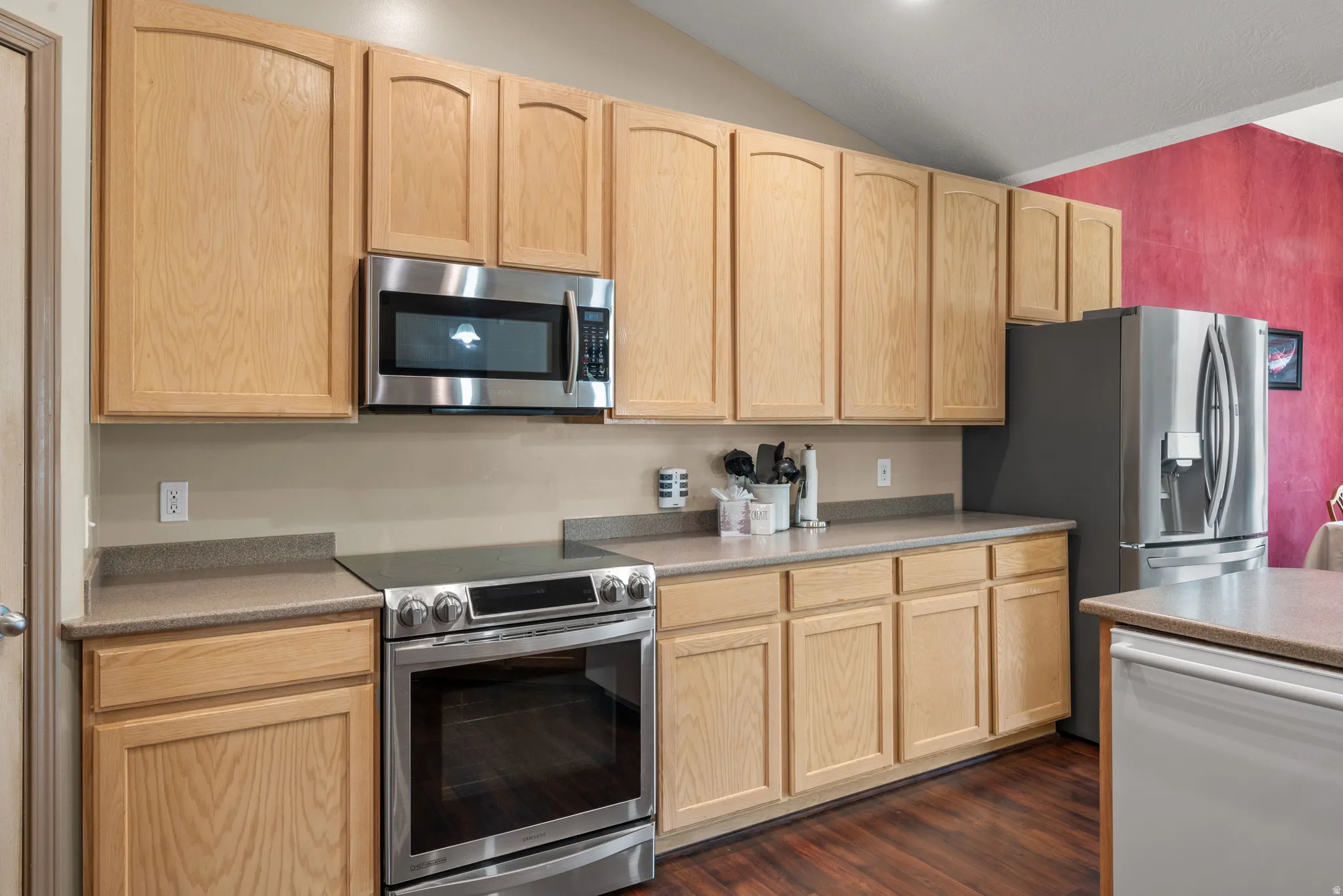 Modern kitchen featuring natural wood cabinetry, stainless steel appliances including a gas range and built-in microwave, gray quartz countertops, and wood-finish flooring throughout