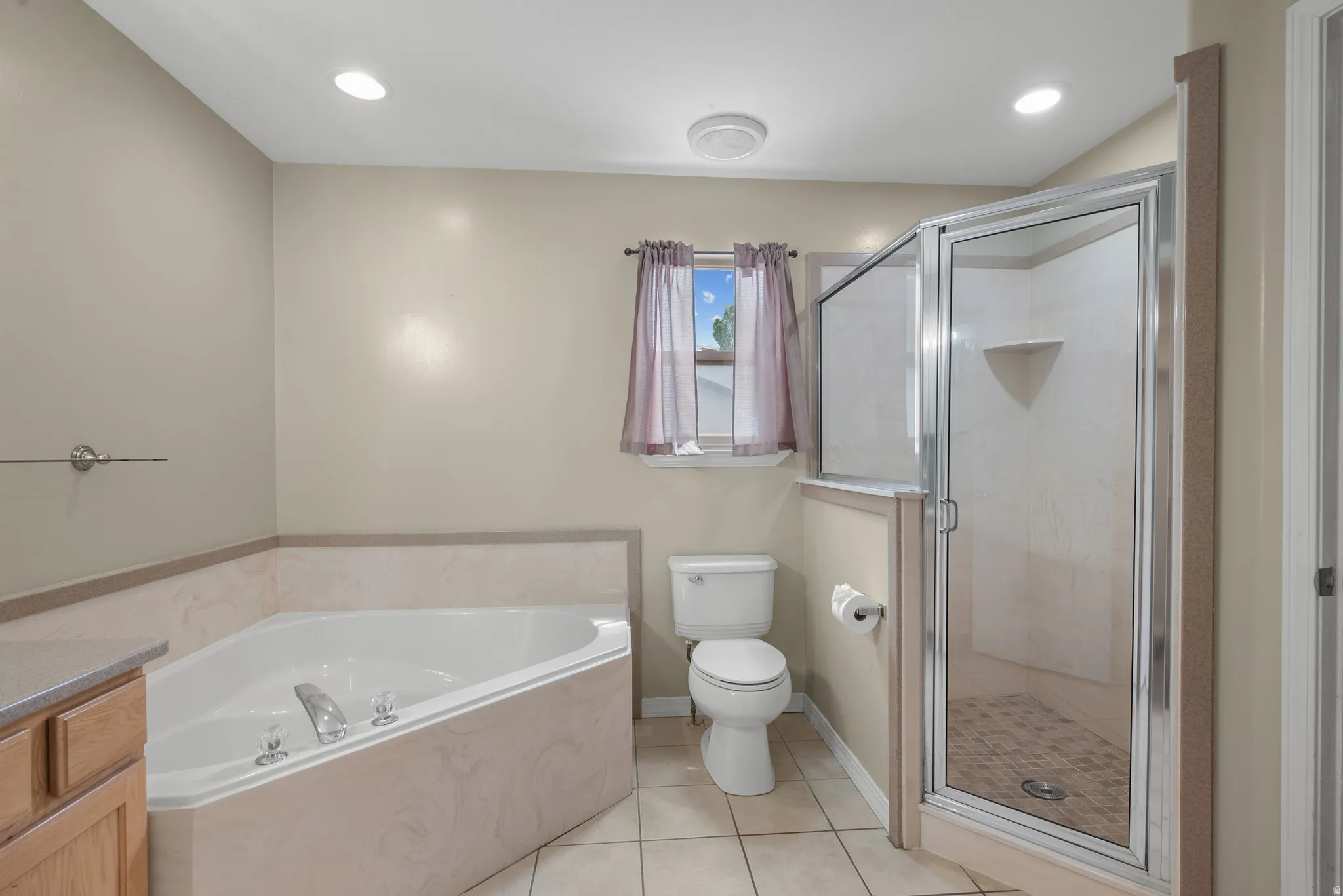 Master bathroom featuring a soaking tub with deck jets, separate walk-in shower with frameless glass enclosure and tile surround, dual vanity with wood cabinetry, and ceramic tile flooring throughout