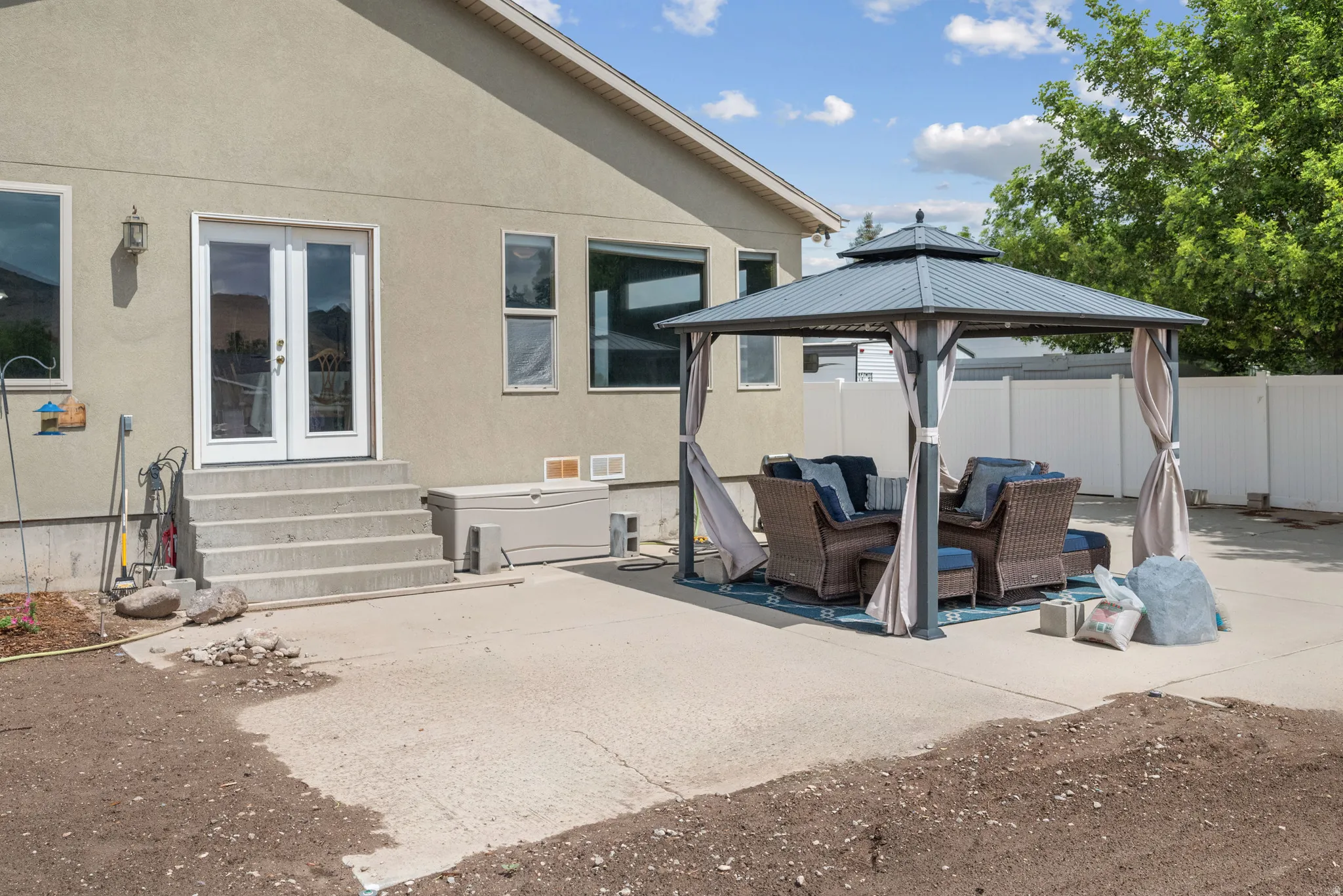 Expansive concrete patio with mature landscaping and privacy fencing, featuring a pergola-style shade structure with integrated seating area