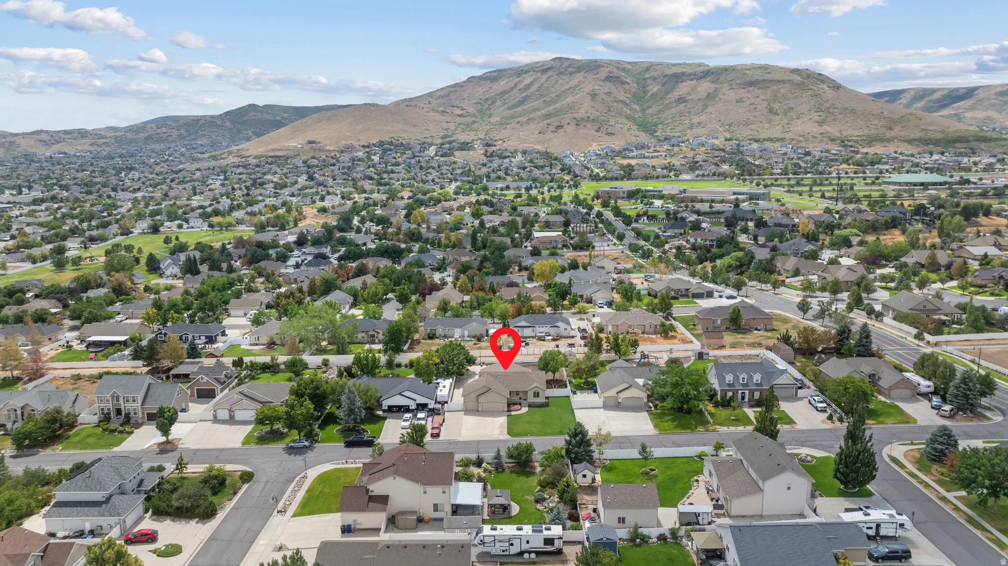 Aerial view showcasing this residential property nestled in an established neighborhood with mature landscaping, tree-lined streets, and mountain backdrop