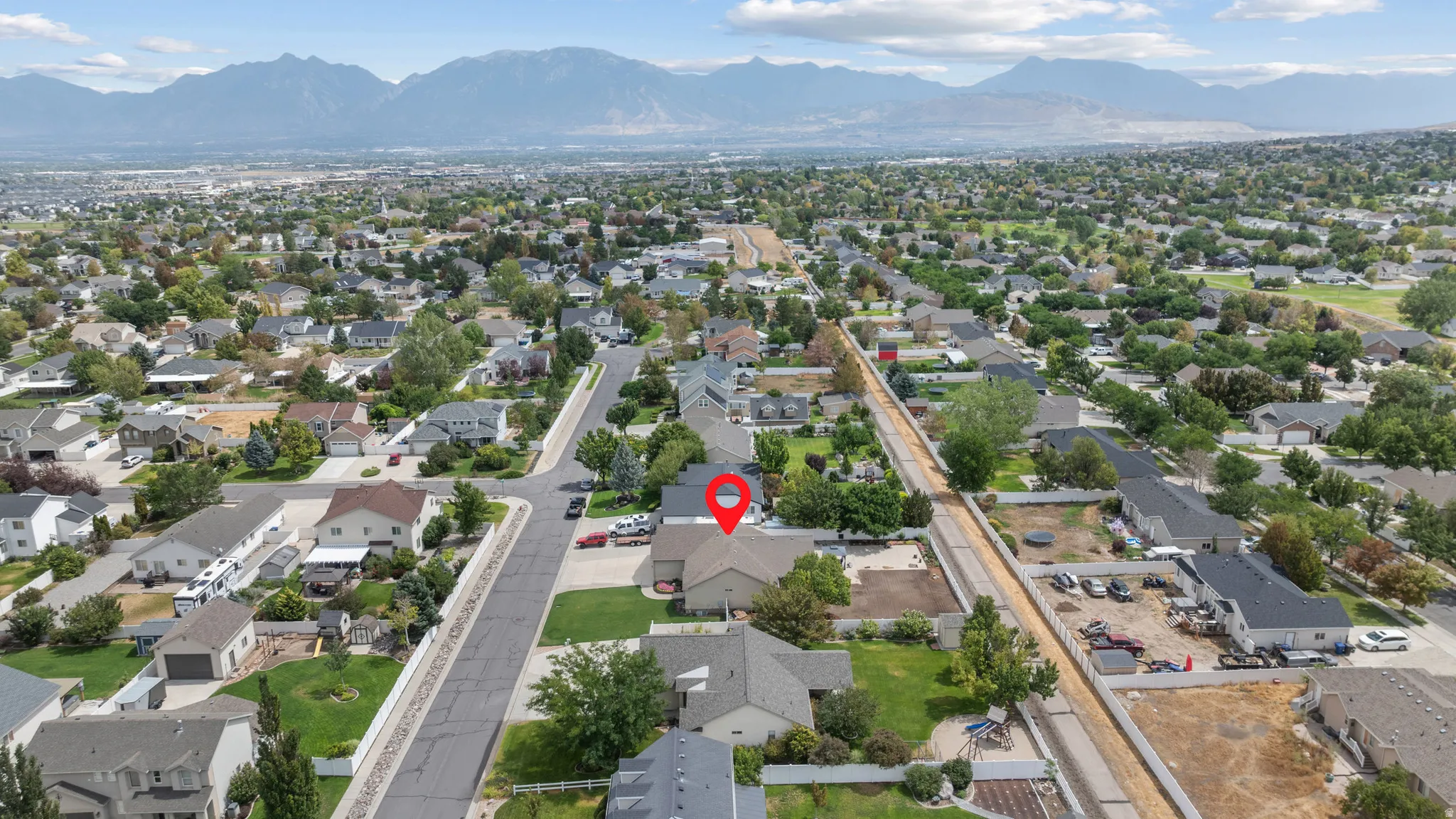 Aerial view showcasing this residential property positioned on a tree-lined street within an established neighborhood, with mountain vistas visible in the distance and mature landscaping throughout the surrounding area