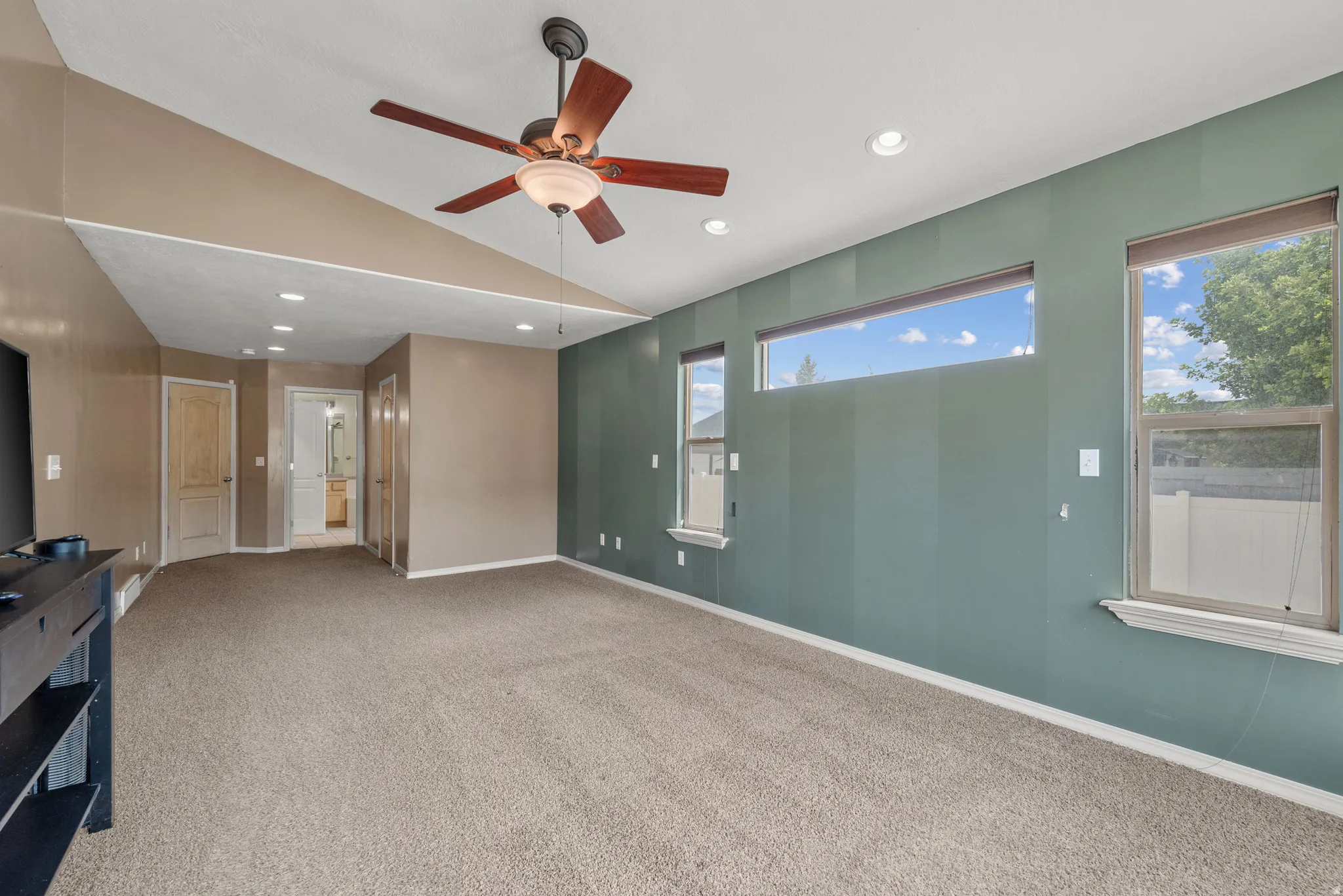 Spacious primary suite featuring neutral carpet flooring, soft recessed lighting, ceiling fan with wood-finish blades, and dual-tone wall treatment with sage green accent wall