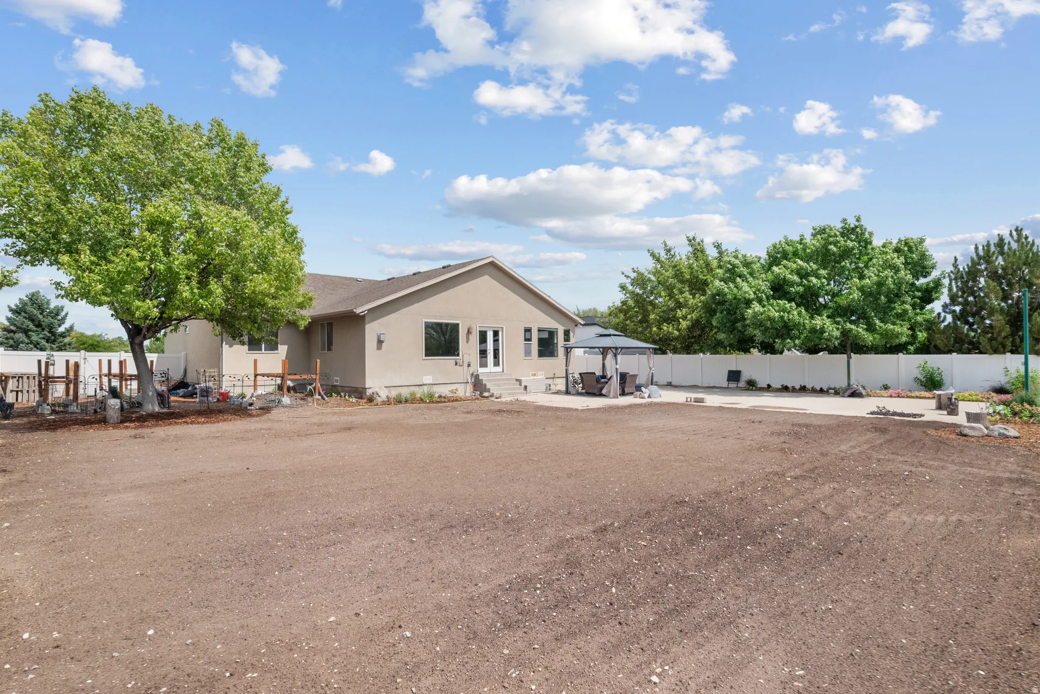 Expansive outdoor area featuring a stucco exterior, concrete patio, and a white privacy fence