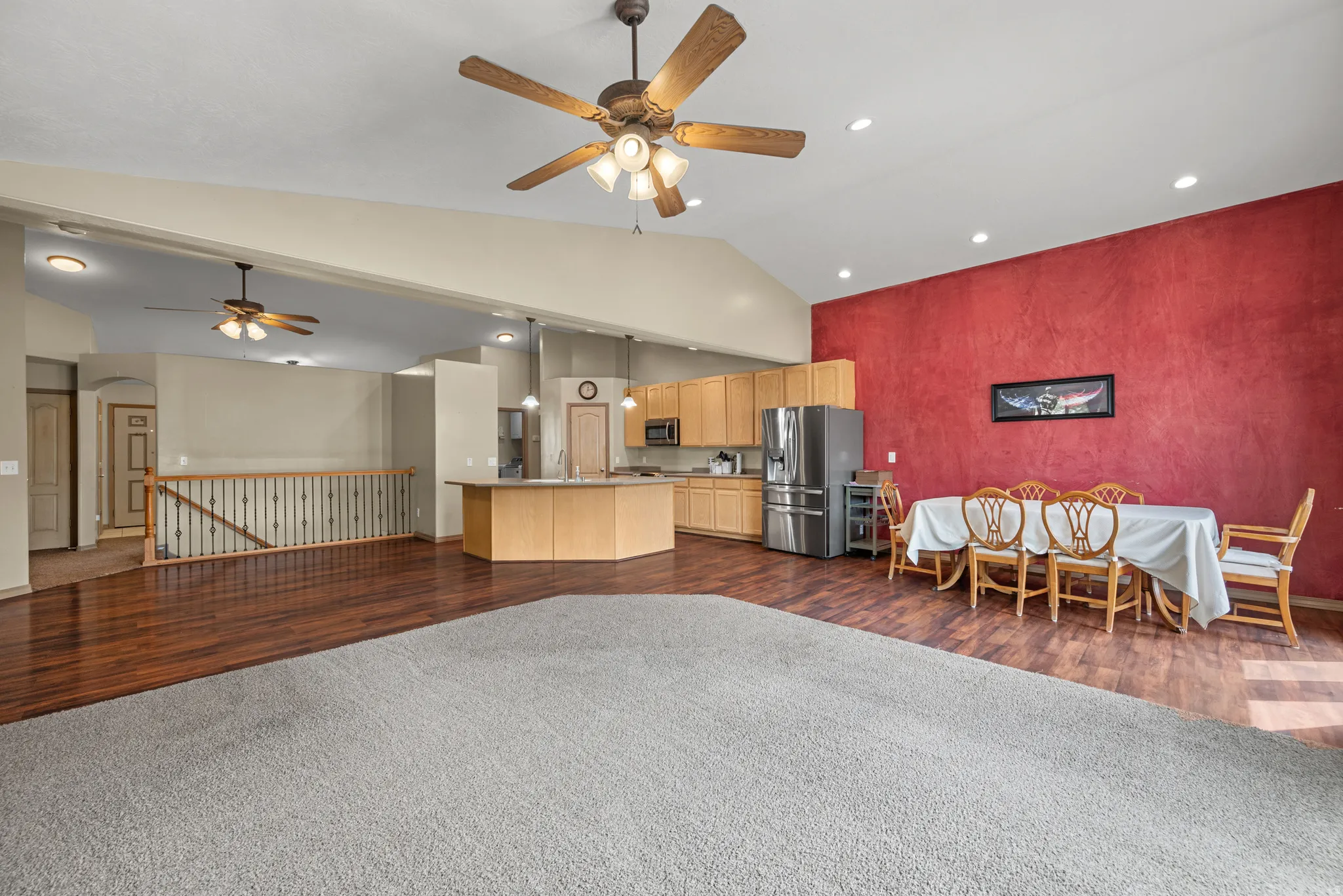 Vaulted ceilings with recessed lighting, wood-finish flooring, kitchen island with counter seating, and light wood cabinetry