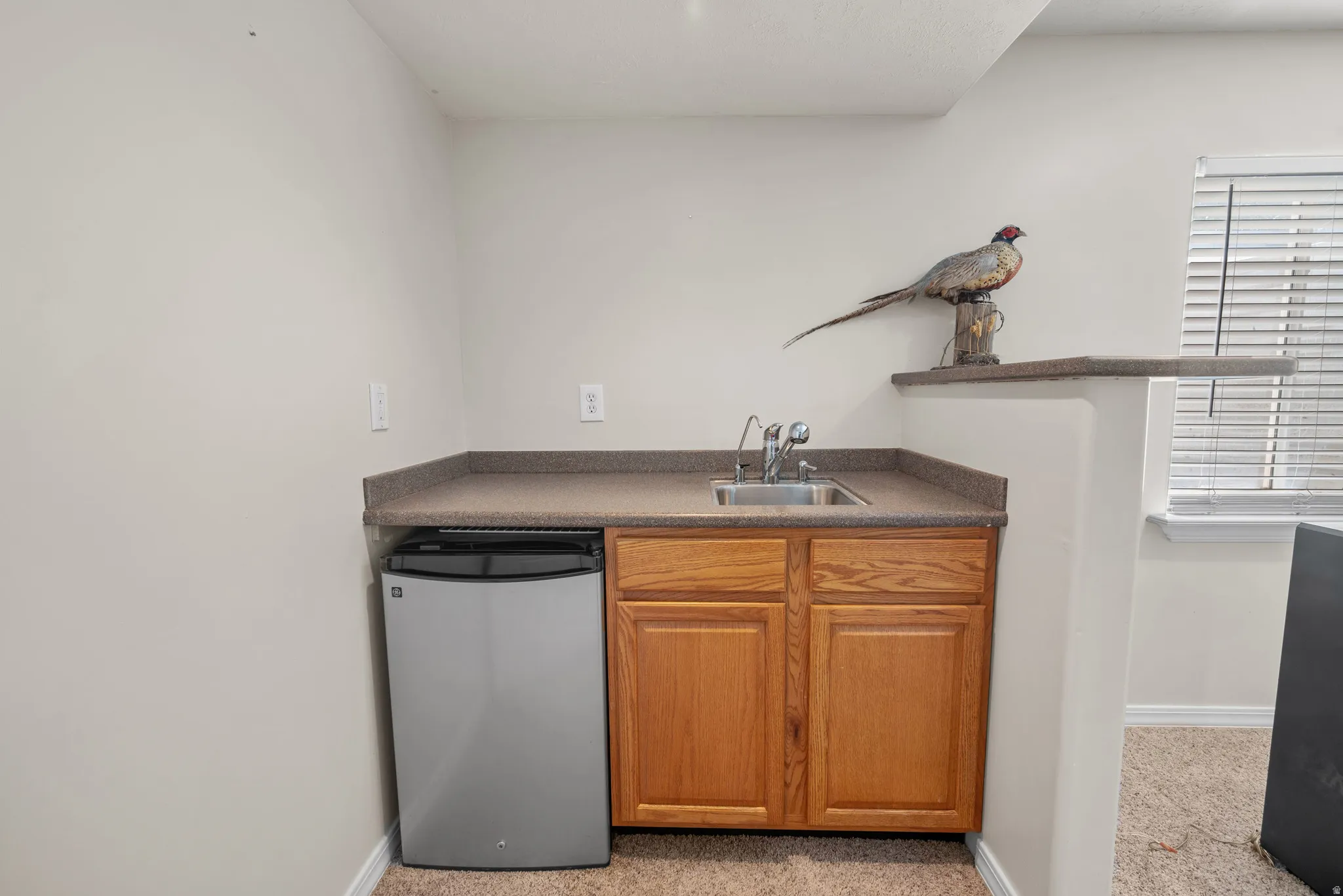 Compact wet bar featuring a stainless steel sink, wood cabinetry, and a built-in refrigerator
