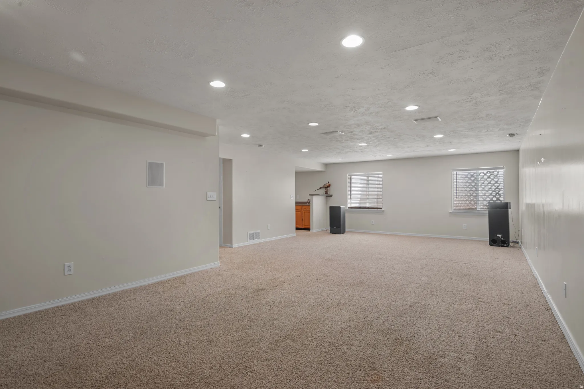 Spacious basement recreation area featuring neutral carpeting throughout, recessed ceiling lighting, and multiple windows providing natural illumination
