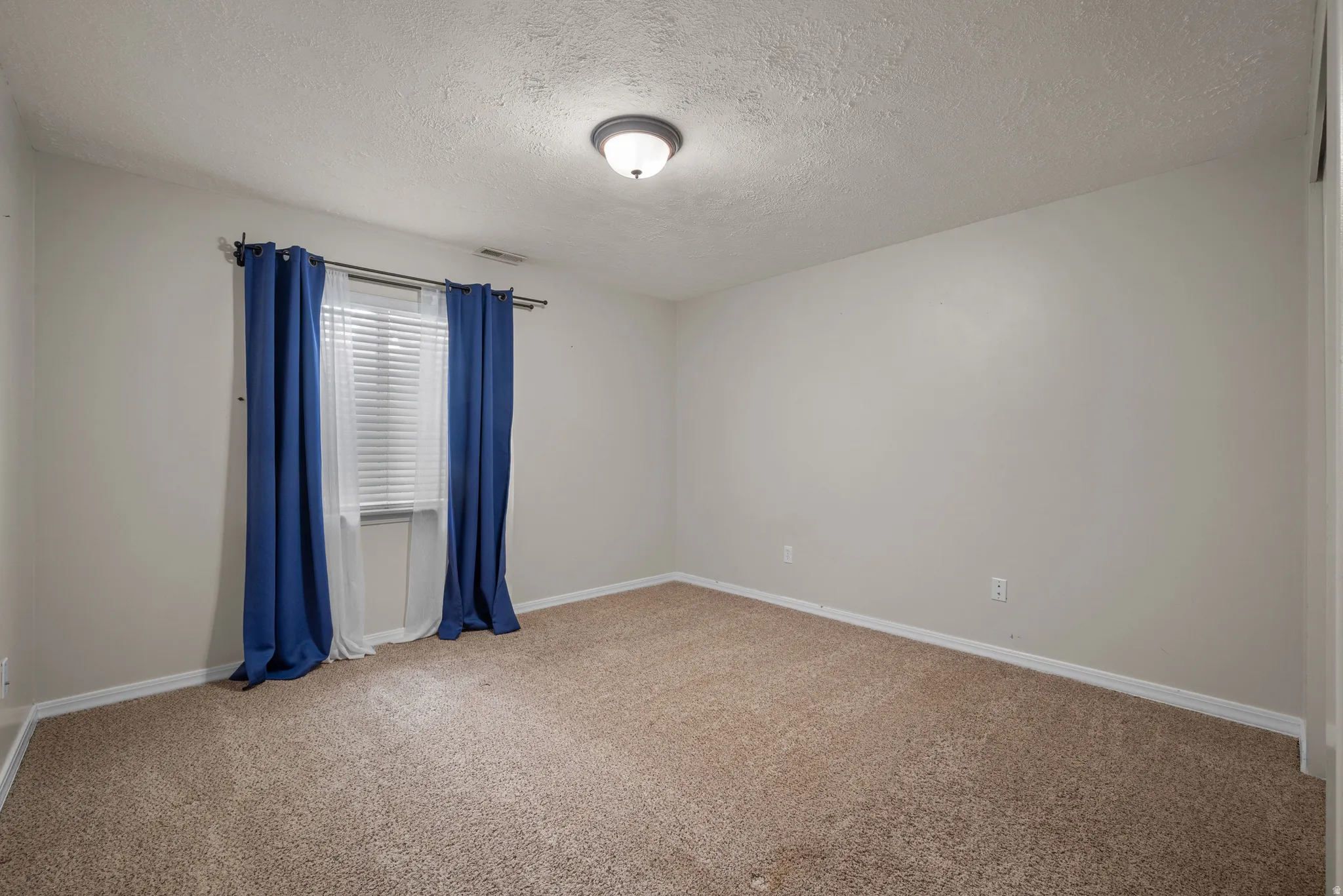 Neutral wall paint, textured ceiling, flush mount ceiling light fixture, window with blinds