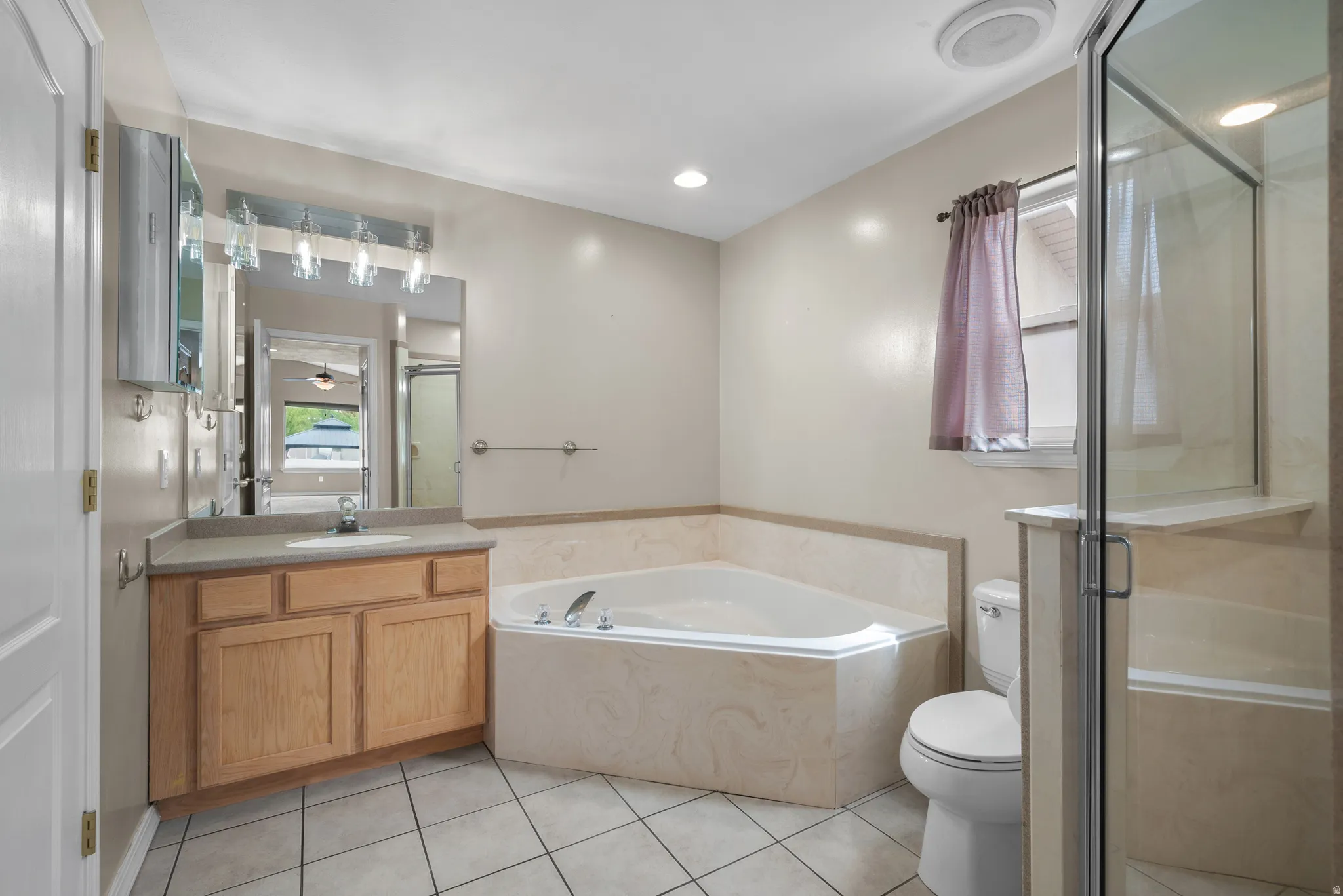 Spa-inspired primary bathroom featuring a soaking tub with tile surround, wood-finish vanity with dual sink configuration, recessed lighting, ceramic tile flooring, and a frameless glass-enclosed shower enclosure with tile walls