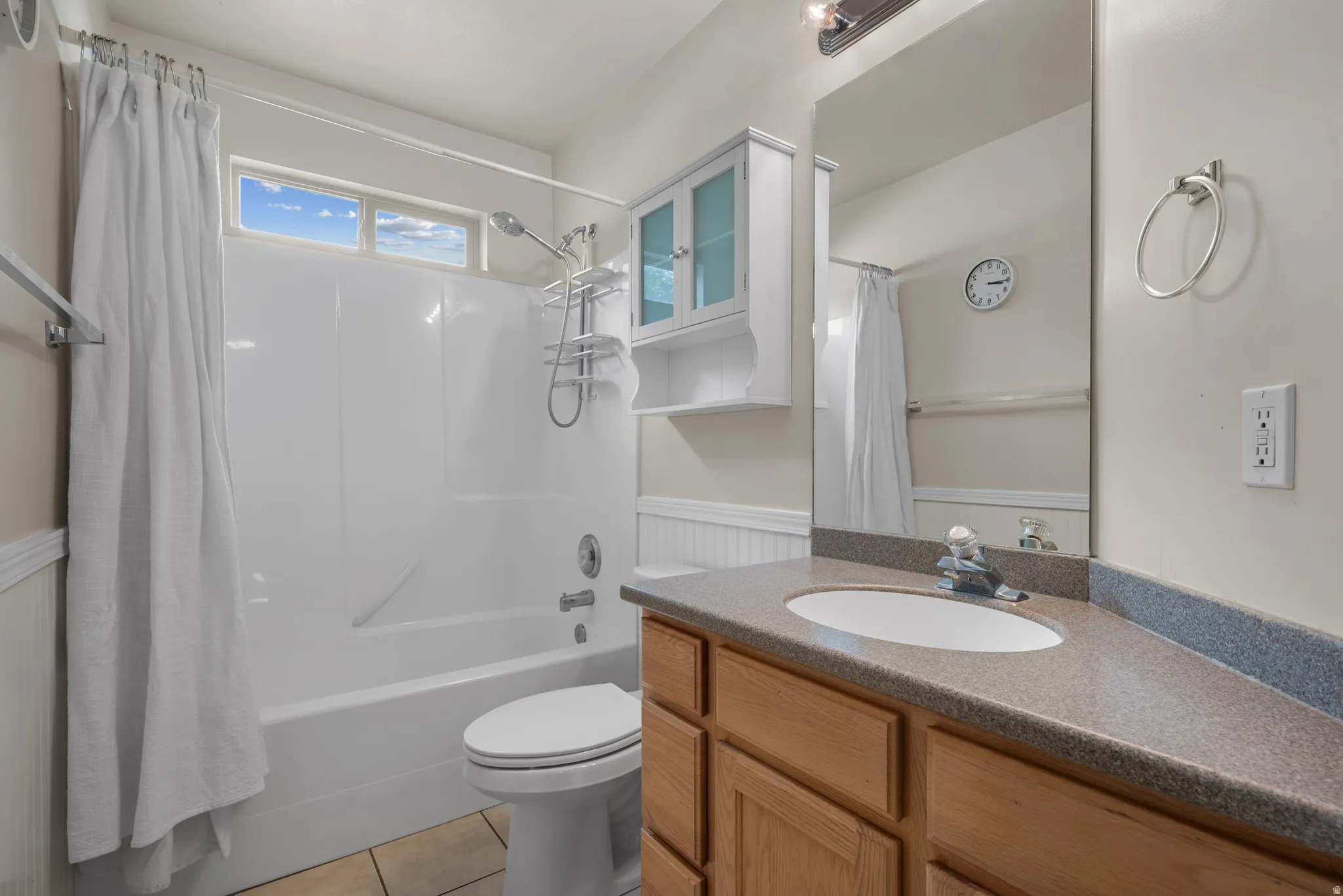 Bathroom featuring a shower-tub combination, wood-finish vanity with an integrated sink, broad wall mirror, and upper window for natural light