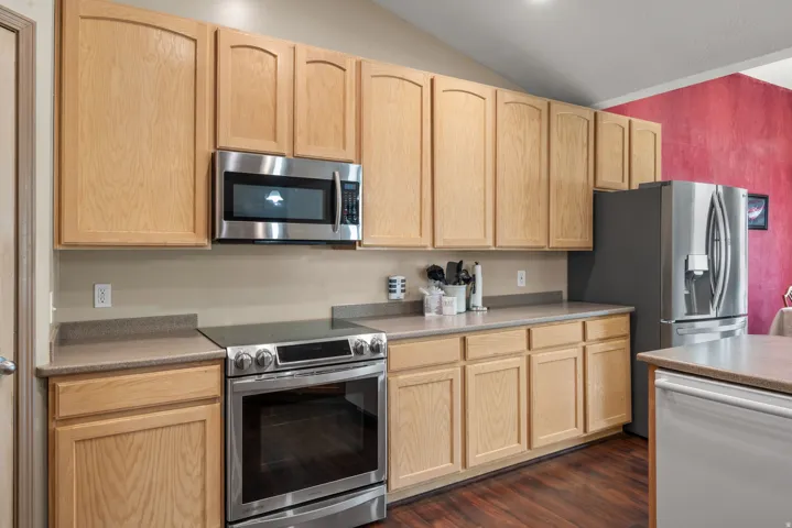 Modern kitchen featuring natural wood cabinetry, stainless steel appliances including a gas range and built-in microwave, gray quartz countertops, and wood-finish flooring throughout