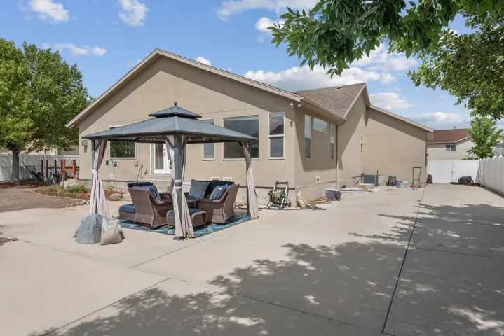 Expansive concrete patio with a permanent gazebo structure, stucco exterior, and a white privacy fence