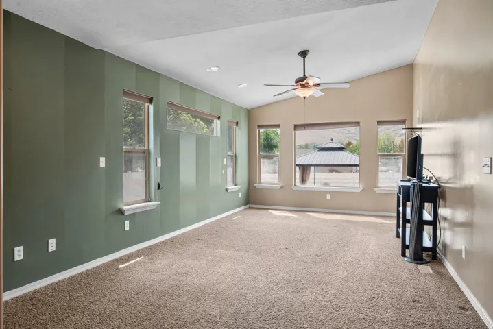 Spacious open room featuring neutral-toned walls, sage green accent wall, recessed ceiling lighting, ceiling fan, and carpet flooring throughout