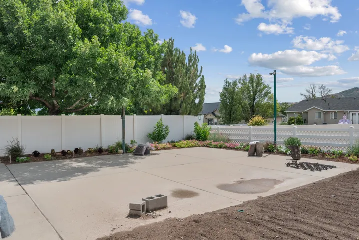 Expansive backyard with mature shade trees, concrete patio, and defined landscaping beds bordered by vinyl fencing