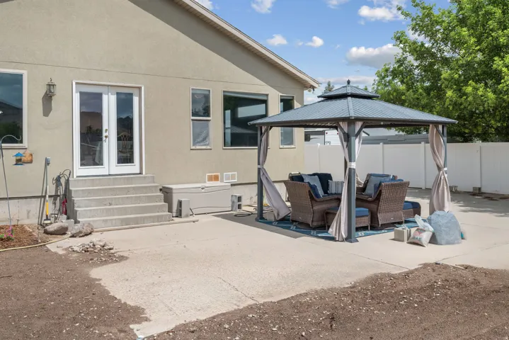 Expansive concrete patio with mature landscaping and privacy fencing, featuring a pergola-style shade structure with integrated seating area