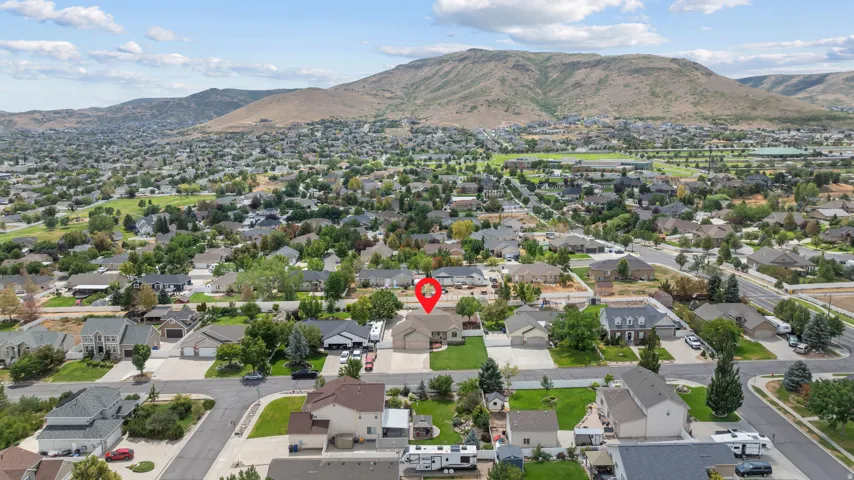Aerial view showcasing this residential property nestled in an established neighborhood with mature landscaping, tree-lined streets, and mountain backdrop