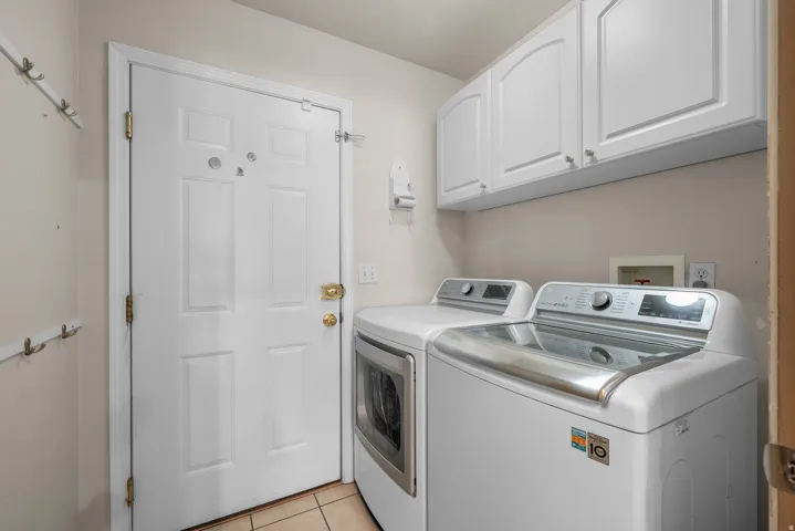 Dedicated laundry area featuring white upper cabinetry, tiled flooring, and a paneled entry door