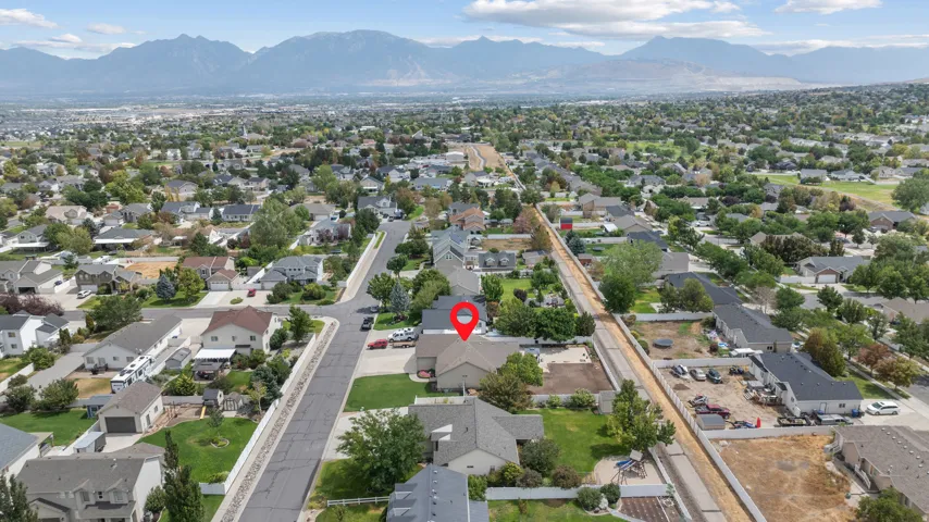 Aerial view showcasing this residential property positioned on a tree-lined street within an established neighborhood, with mountain vistas visible in the distance and mature landscaping throughout the surrounding area