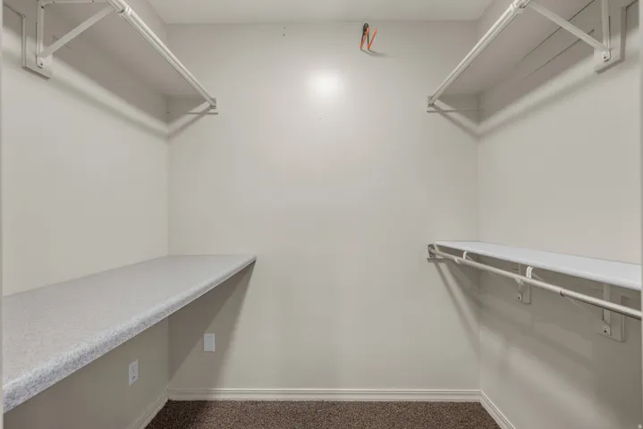 Spacious walk-in closet featuring dual built-in shelving units with granite-finish countertops, professional LED lighting systems, and polished metal hardware and rods for optimal organization and storage capacity