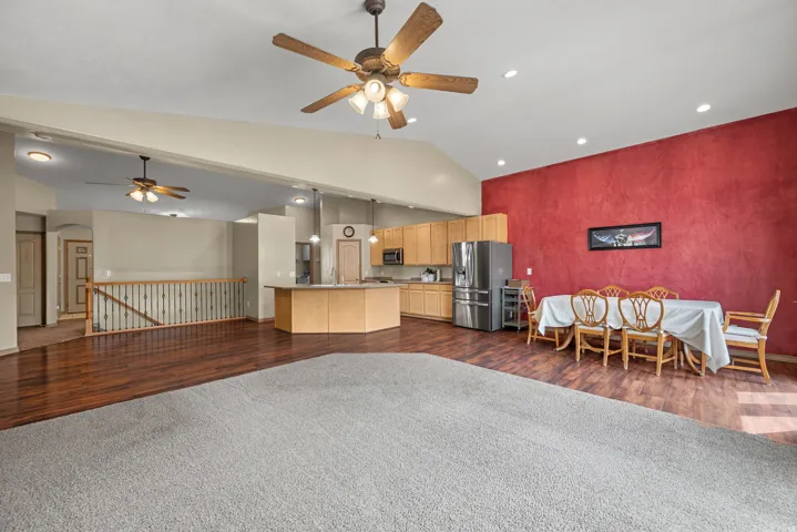 Vaulted ceilings with recessed lighting, wood-finish flooring, kitchen island with counter seating, and light wood cabinetry