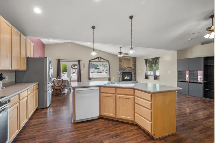 Spacious open-concept kitchen featuring wood cabinetry, stainless steel appliances, a large center island with wood-finish base, white quartz countertops, pendant lighting, and wood-finish flooring throughout