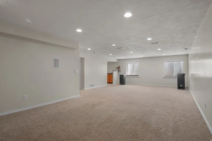 Spacious basement recreation area featuring neutral carpeting throughout, recessed ceiling lighting, and multiple windows providing natural illumination