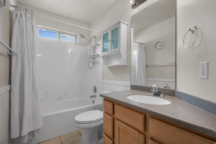Bathroom featuring a shower-tub combination, wood-finish vanity with an integrated sink, broad wall mirror, and upper window for natural light