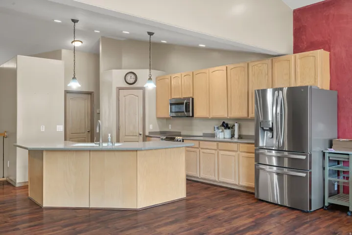 Kitchen featuring a stainless steel refrigerator, microwave, wood-finish flooring, and light-toned cabinetry
