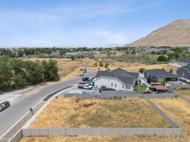 Expansive open lot featuring a perimeter fence, paved road frontage, and distant mountain scenery