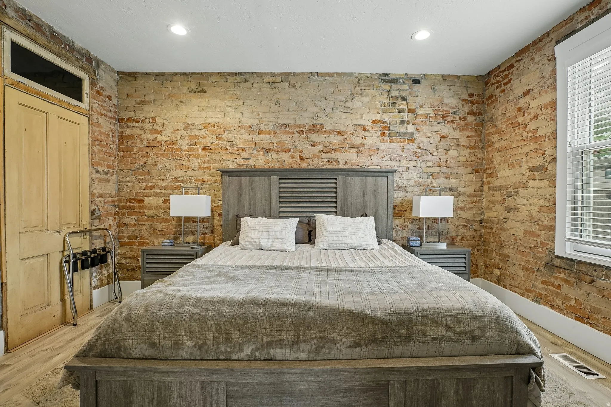 Exposed brick walls, recessed ceiling lighting, wood-finish flooring, and a large window with blinds