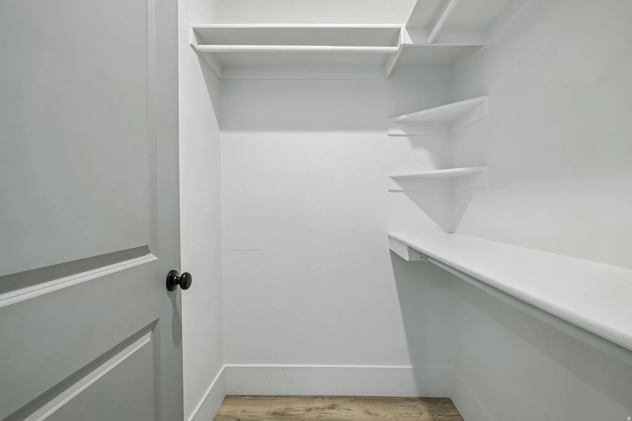 Spacious walk-in closet featuring custom white shelving and cabinetry, integrated LED lighting, and wood-finish flooring throughout