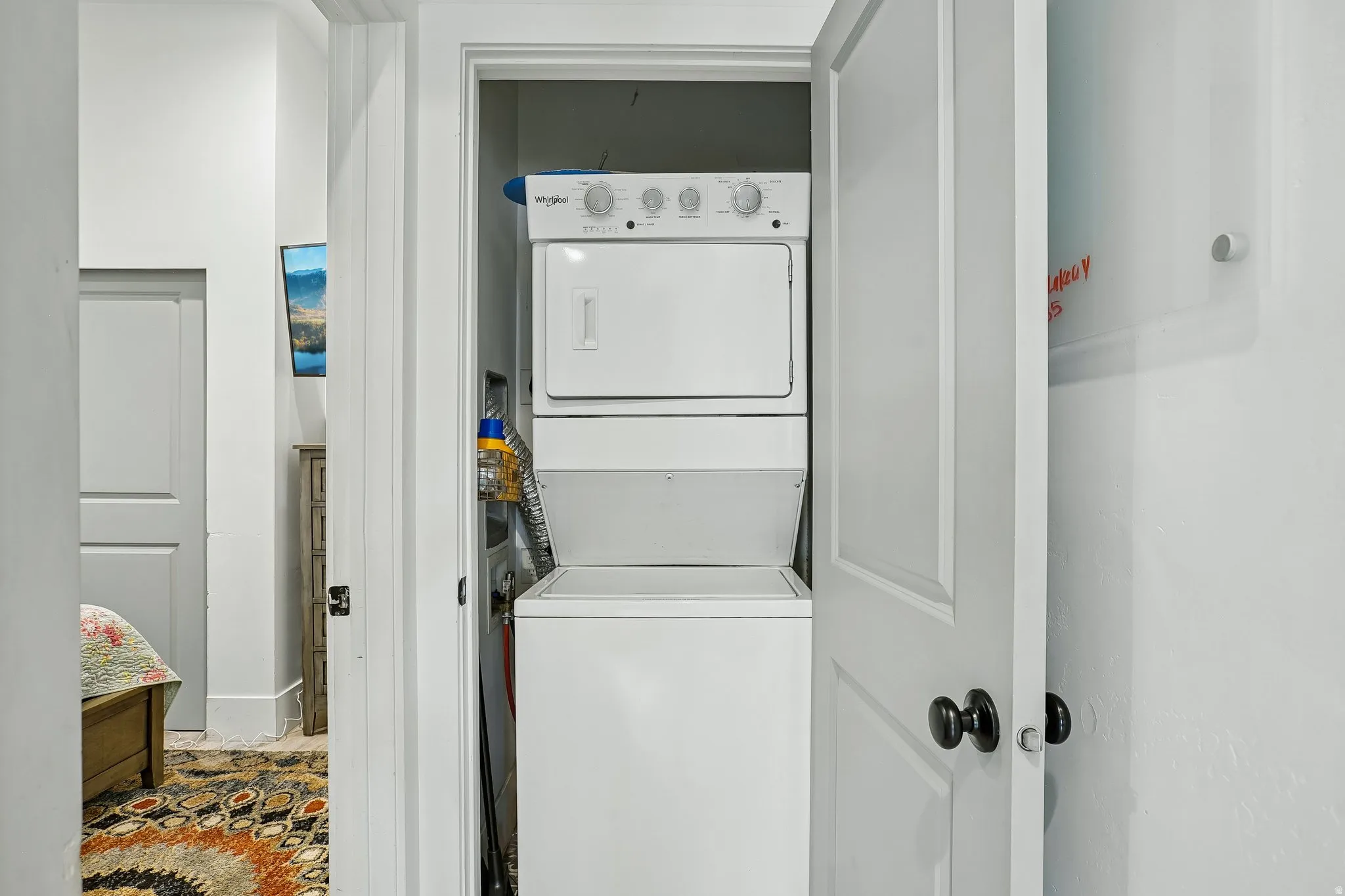 In-unit stacked washer and dryer with white finish and control panel, positioned within a dedicated laundry closet featuring white painted walls and framed doorway access