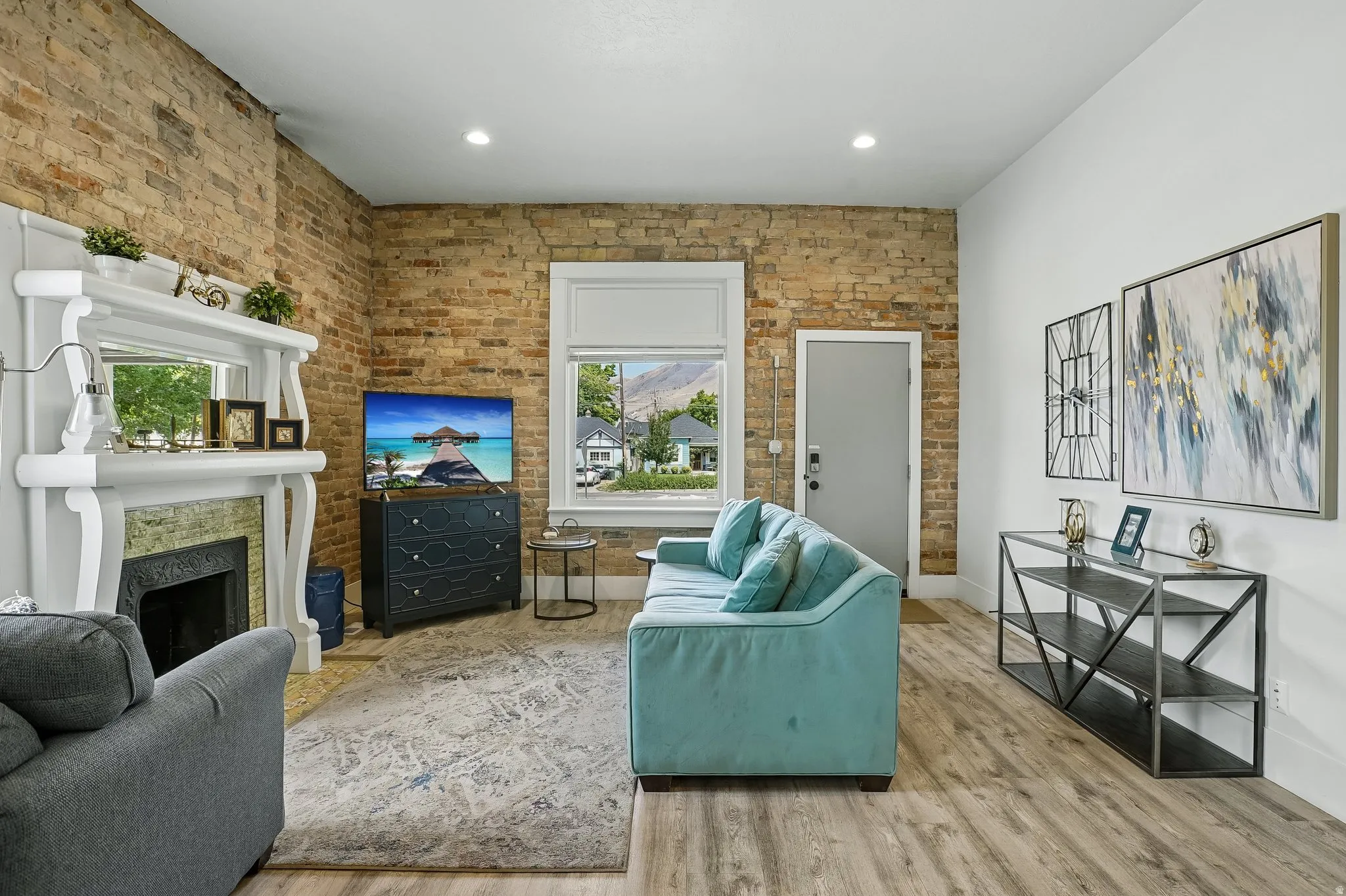 Bright living room showcasing exposed brick accent wall, wood-finish flooring, and recessed lighting throughout