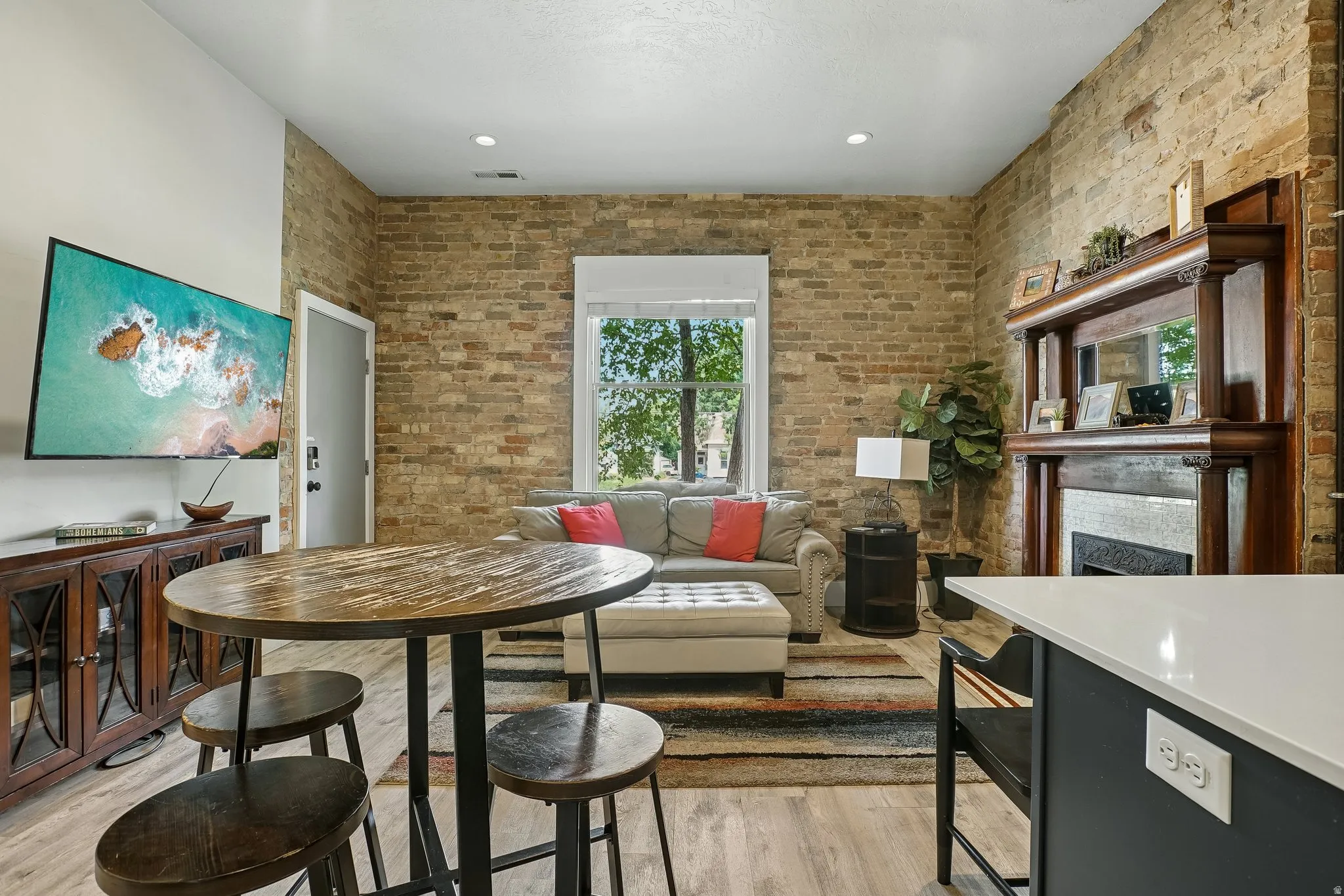 Open-concept living area featuring exposed brick walls, recessed ceiling lighting, and wood-finish flooring