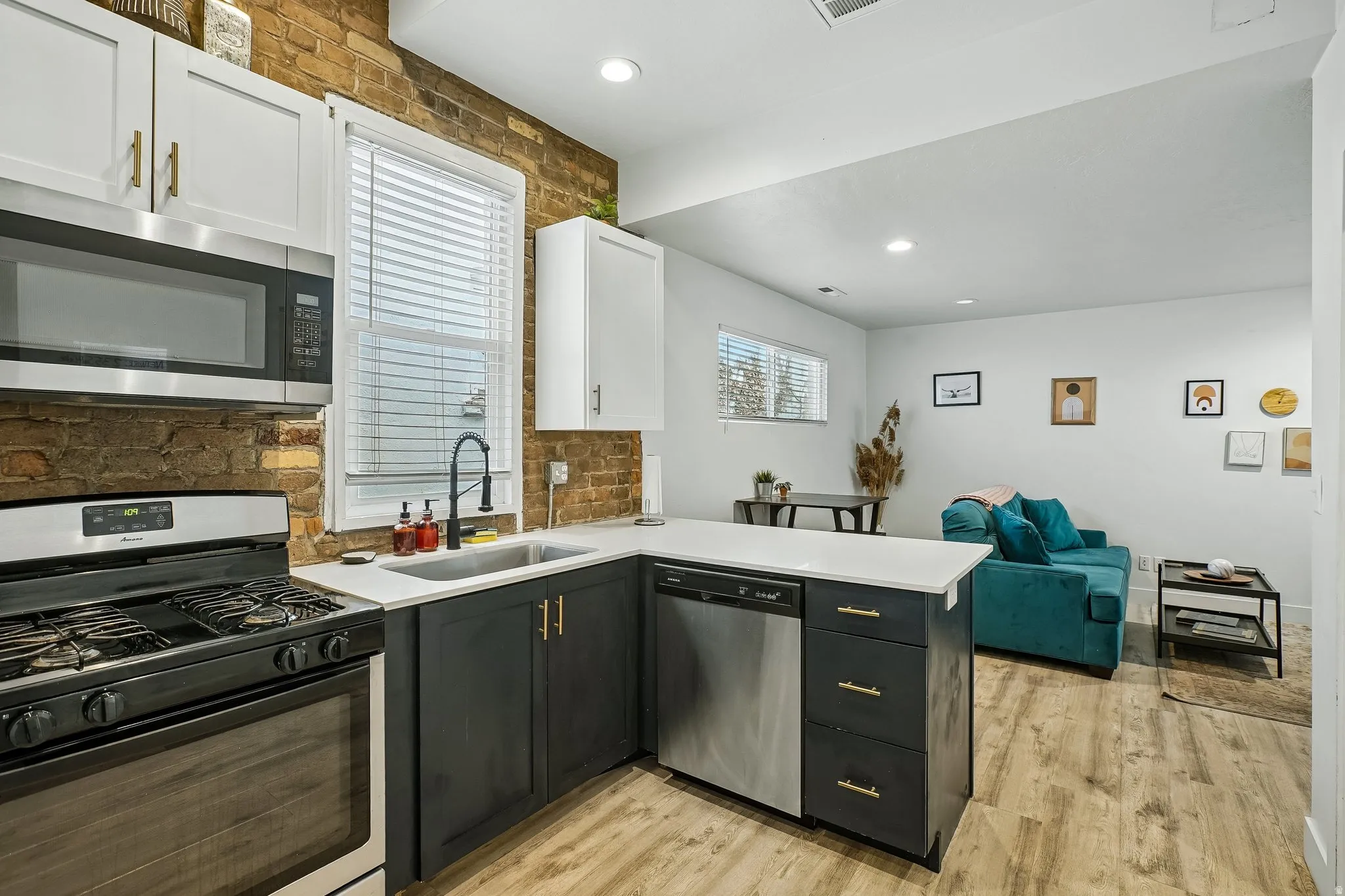 Modern kitchen featuring stainless steel appliances, gas range with black cabinetry and brass hardware, white upper cabinets, brick backsplash, white quartz countertops, and wood-finish flooring throughout
