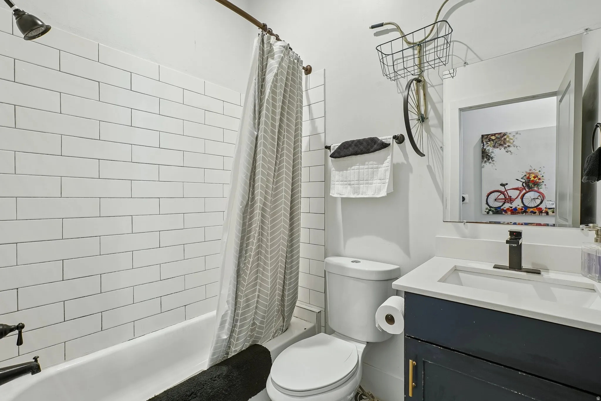 Modern bathroom featuring subway tile walls, a white porcelain vanity with integrated sink, quartz countertop, matte black faucet, and a bathtub with coordinating shower enclosure and neutral patterned curtain