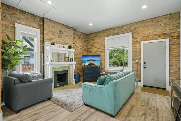 Inviting living room showcasing exposed brick walls, wood-finish flooring, and abundant natural light from multiple windows and glass doors