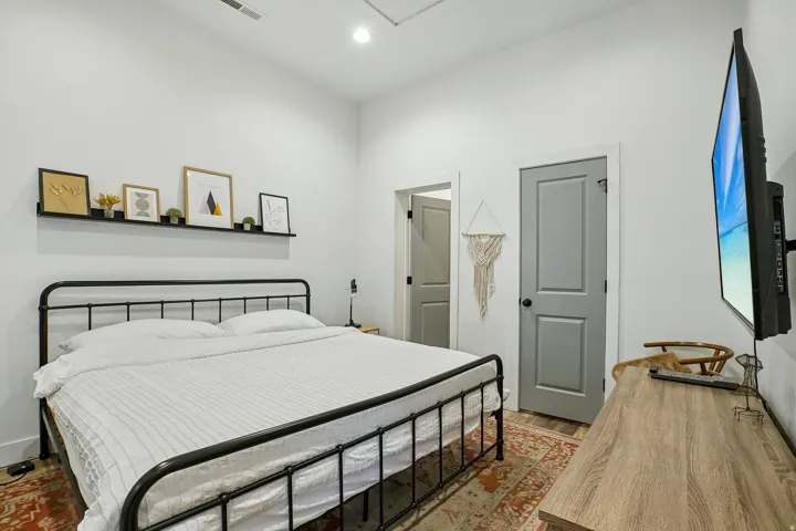 Spacious bedroom featuring a black metal bed frame, white bedding, wood-finish flooring, and warm lighting throughout