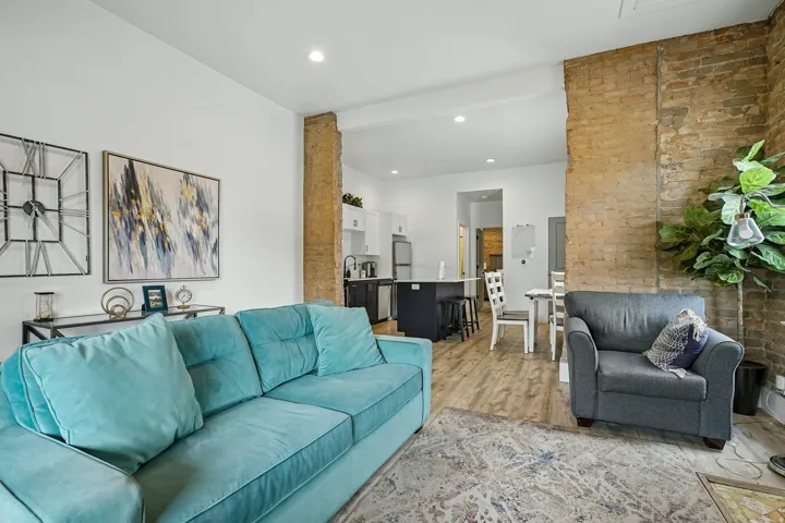 Open-concept living area featuring exposed brick columns, recessed ceiling lighting, and wood-finish flooring throughout