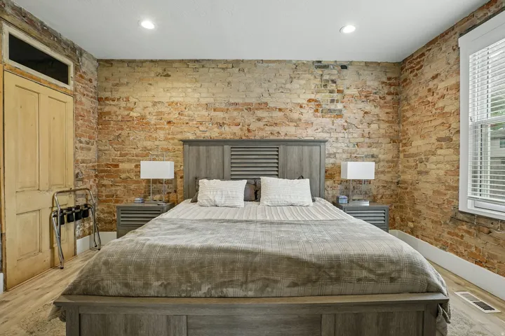 Exposed brick walls, recessed ceiling lighting, wood-finish flooring, and a large window with blinds